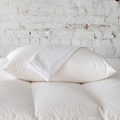 St. Genève Allergy Pillow Protectors stacked on a bed against a white brick wall