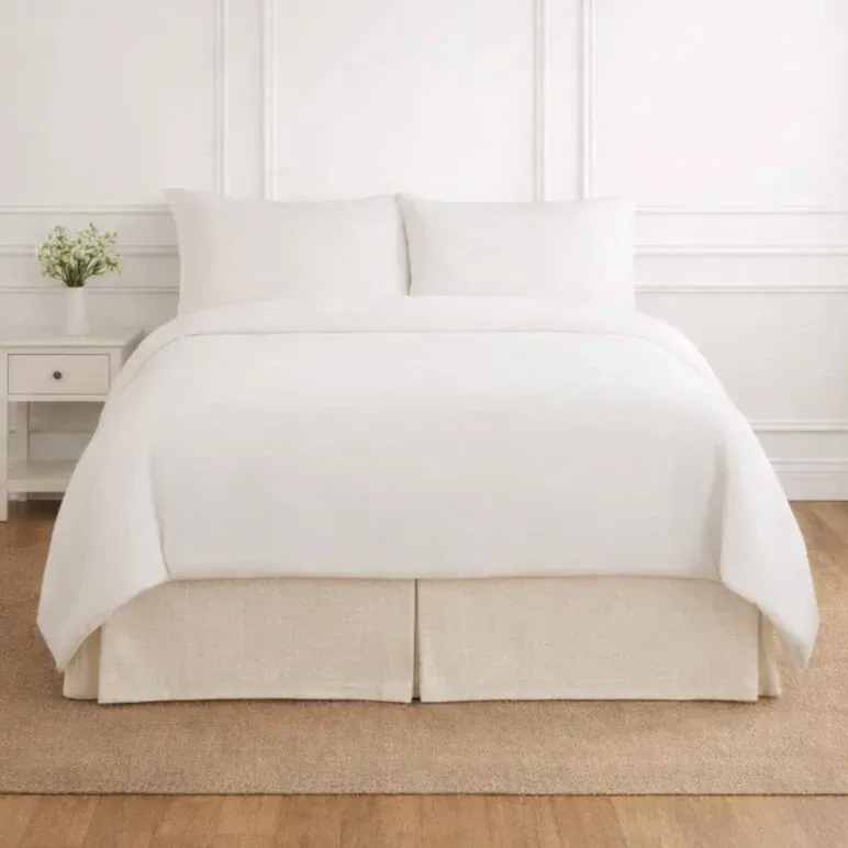 Ann Gish Basketweave tailored bed skirt in natural linen, styled on a bed in a white bedroom.
