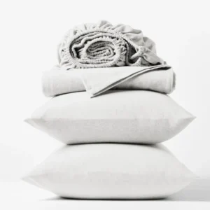 Coyuchi Cloud Brushed Flannel sheet set in white, stacked with pillows and folded sheets.