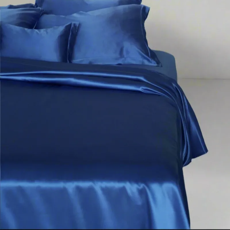 Kumi Kookoon Classic silk sheet set in sapphire blue on a styled bed with pillows.